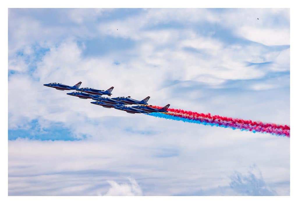 Passage de la Patrouille de France laissant des fumées bleues et rouges dans le ciel